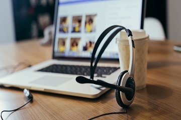 A headset, laptop and coffee cup on a desk.