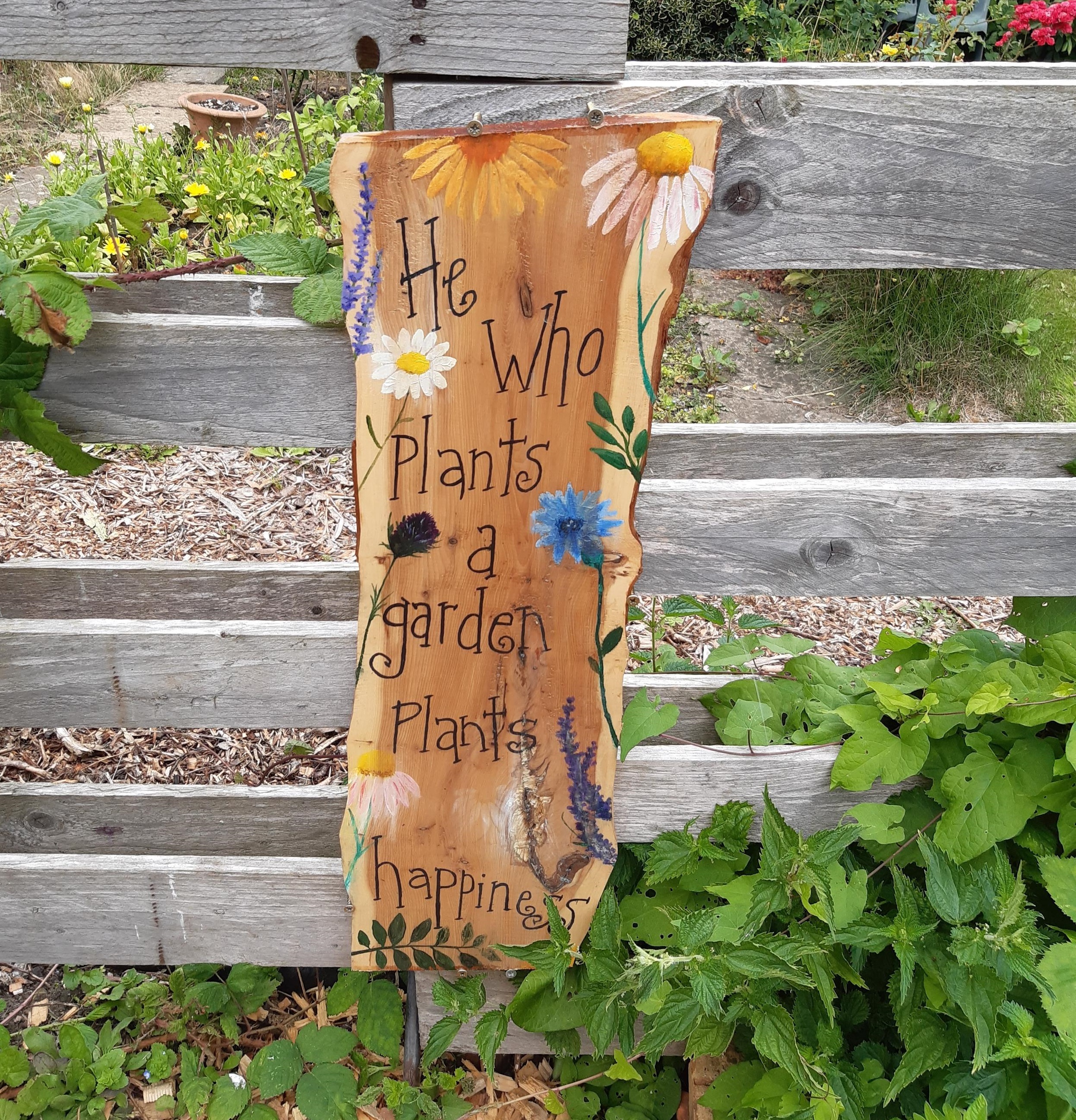 Sign on a fence reading "He who plants a garden plants happiness"