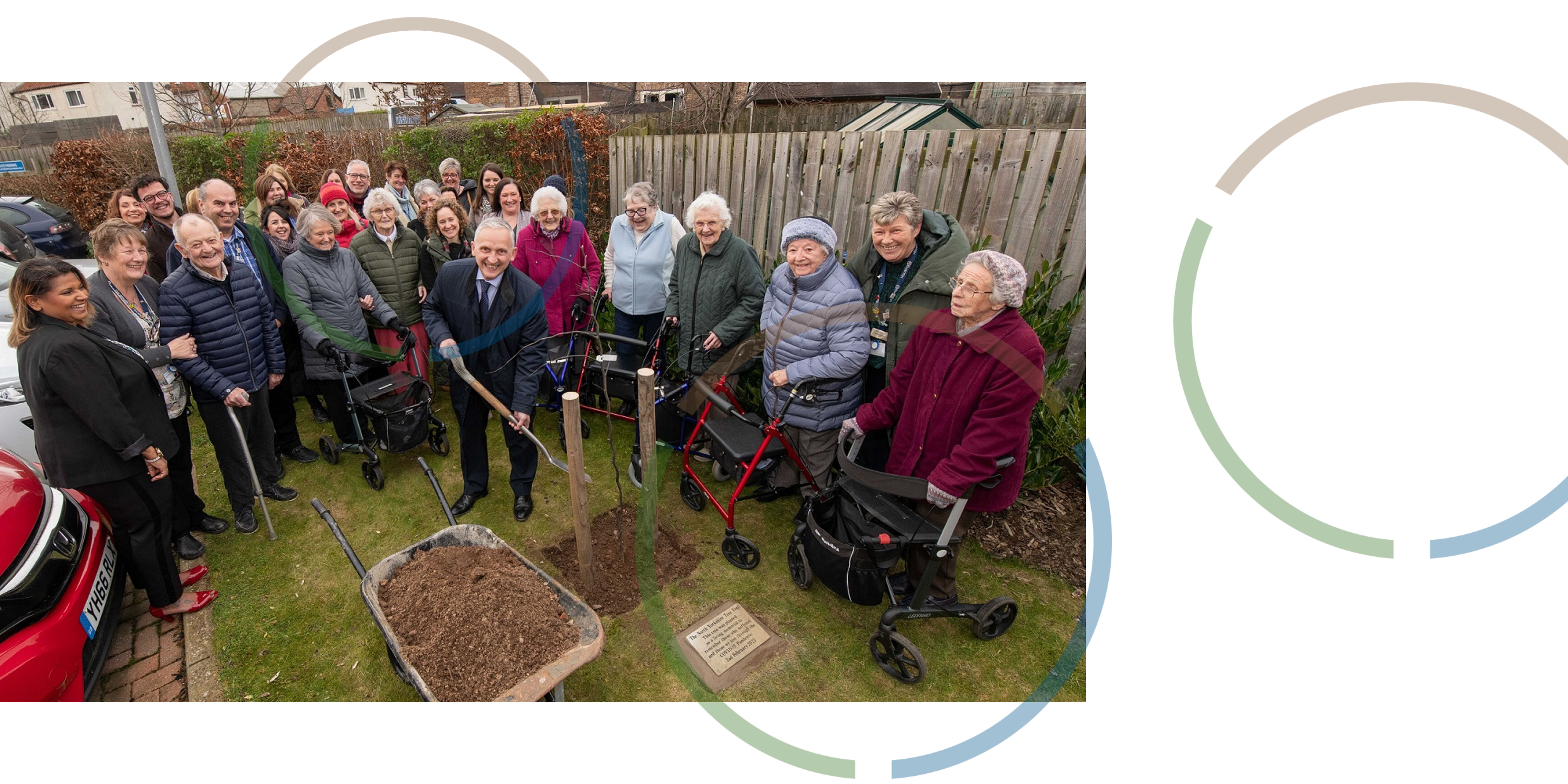 A group of people smiling at a man who is planting a tree.