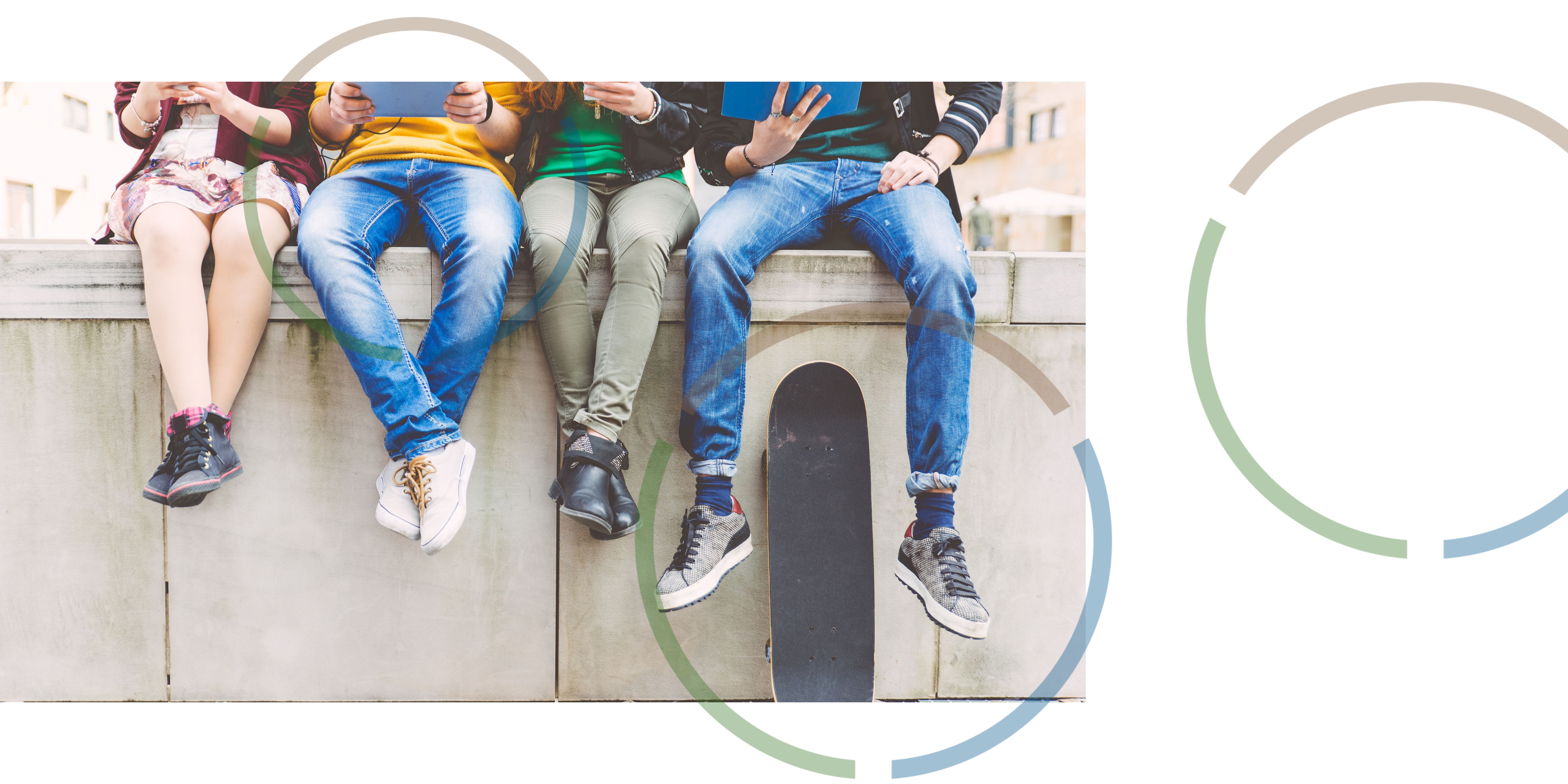 Young people holding tablets and sitting on a wall.