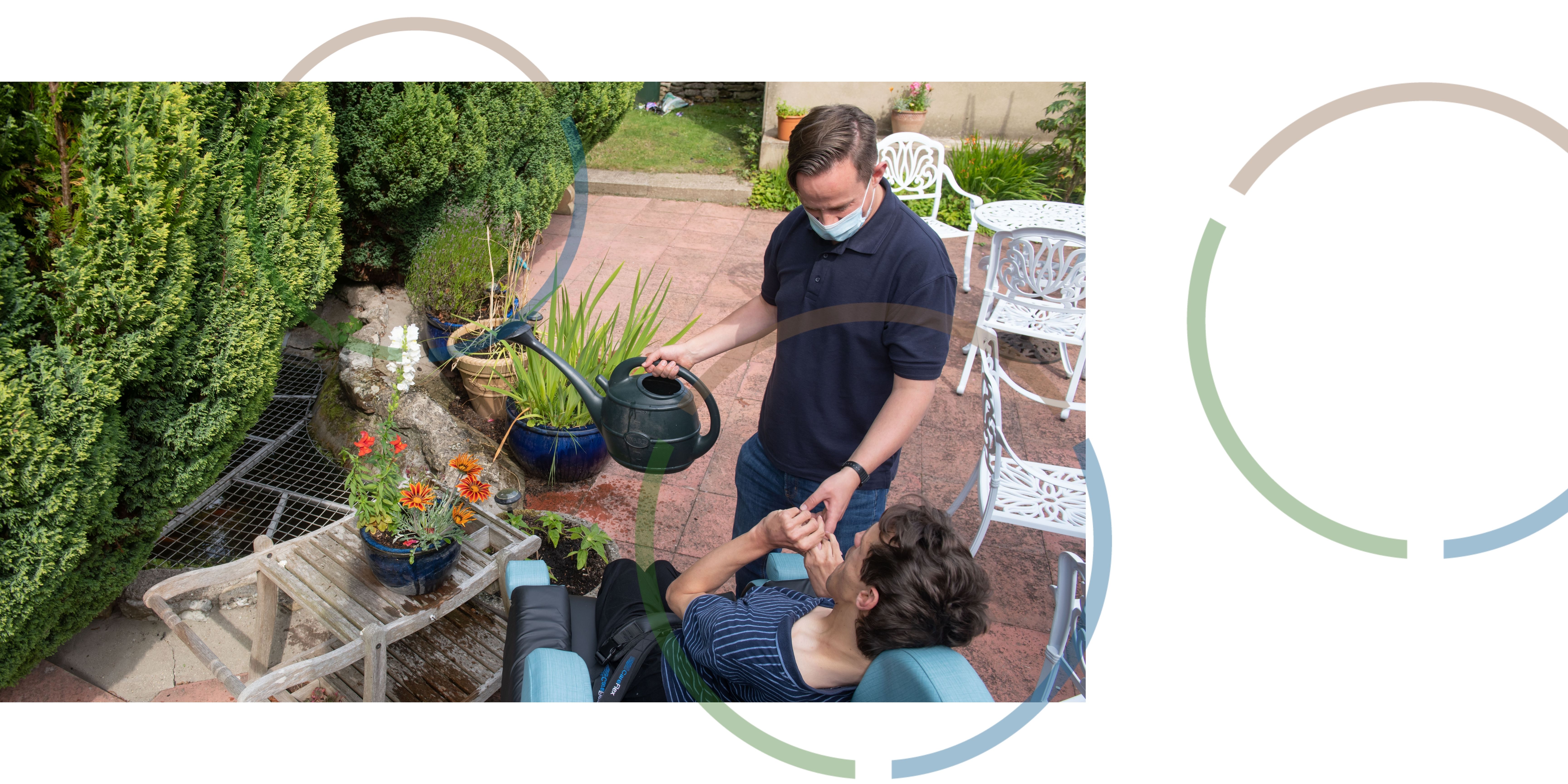 A man wearing a face mask helping a man in a chair to water plants.