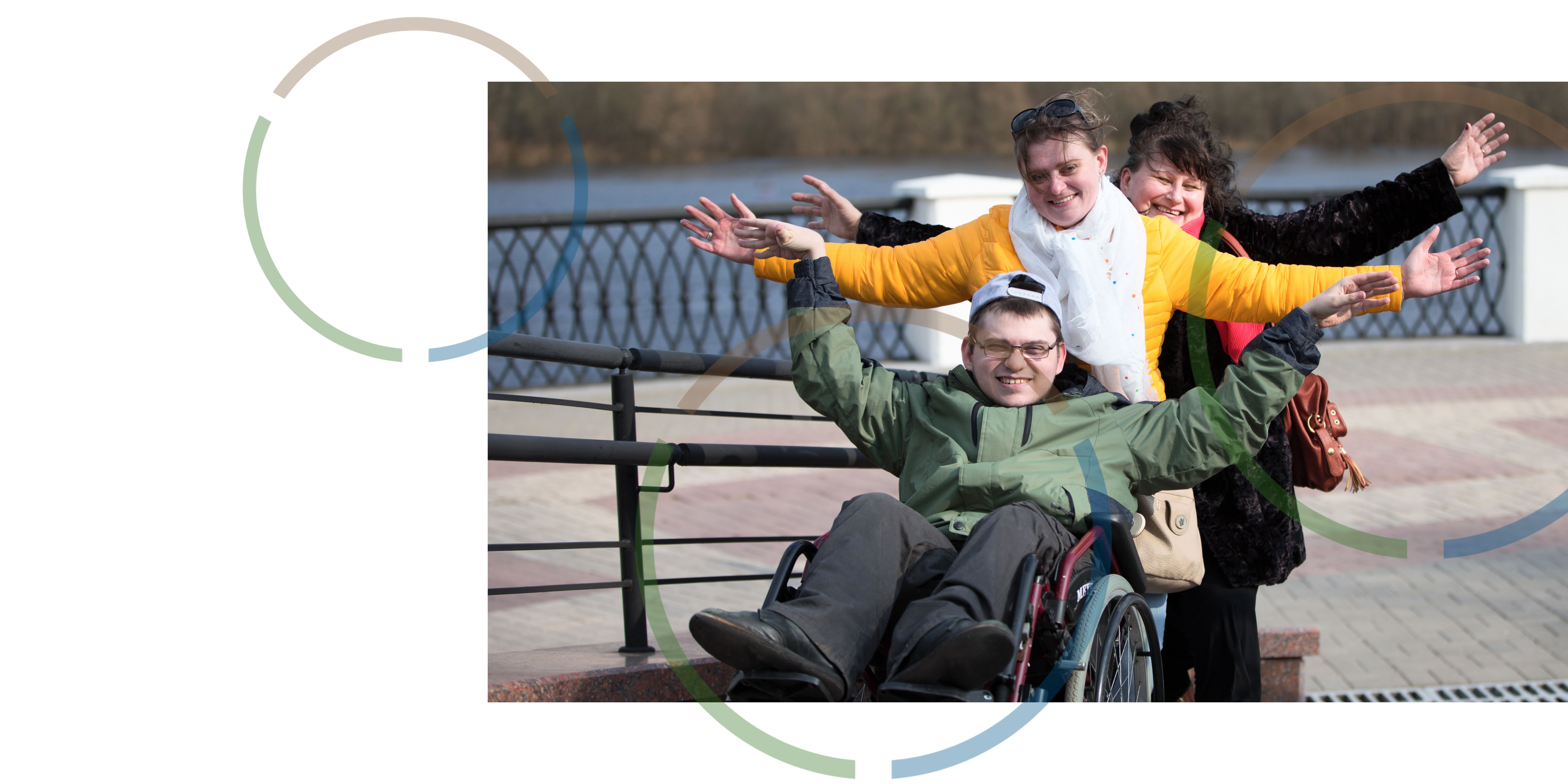 Two woman standing behind a man in a wheelchair. 