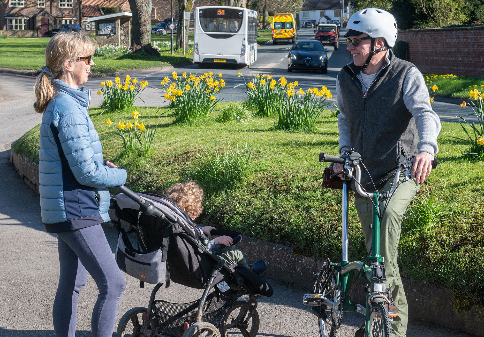 A lady with pushchair talking to a man with a bike