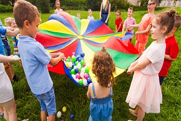 Children playing outside with colourful fabric and plastic balls.