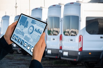 Hands holding a tablet in front of a row of vans.