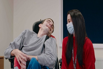 A woman wearing a face mask talking with a man in a wheelchair.