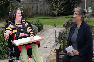 A woman sitting on a bench and a woman in a wheelchair talking and laughing.