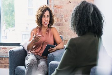 Two women talking in a room with a large window.