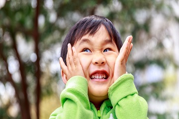 A child smiling with their hands on either side of their face.