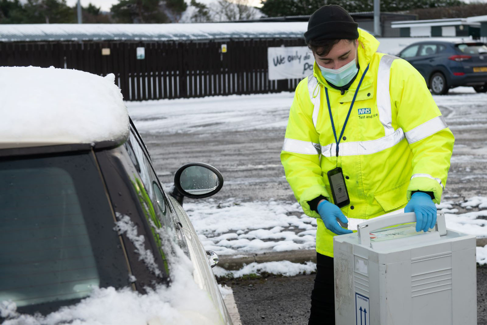 A COVID-19 testing station worker wearing a mask and high vis jacket.