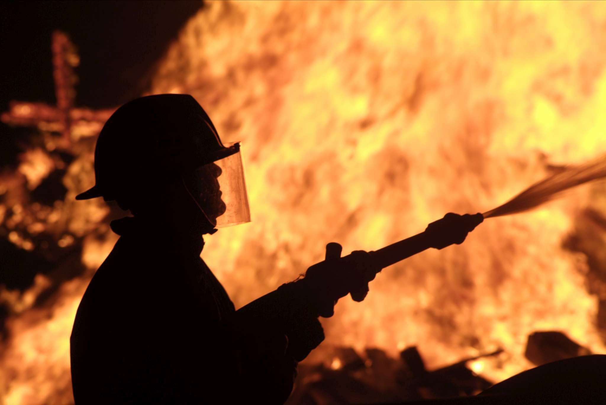 A silhouette of a firefighter spraying water onto a large blaze.