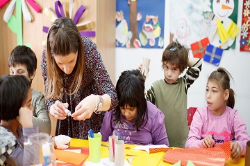 A woman helping children with arts and crafts in a classroom.