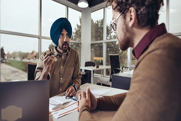 Two men talking in a bright office over paperwork.