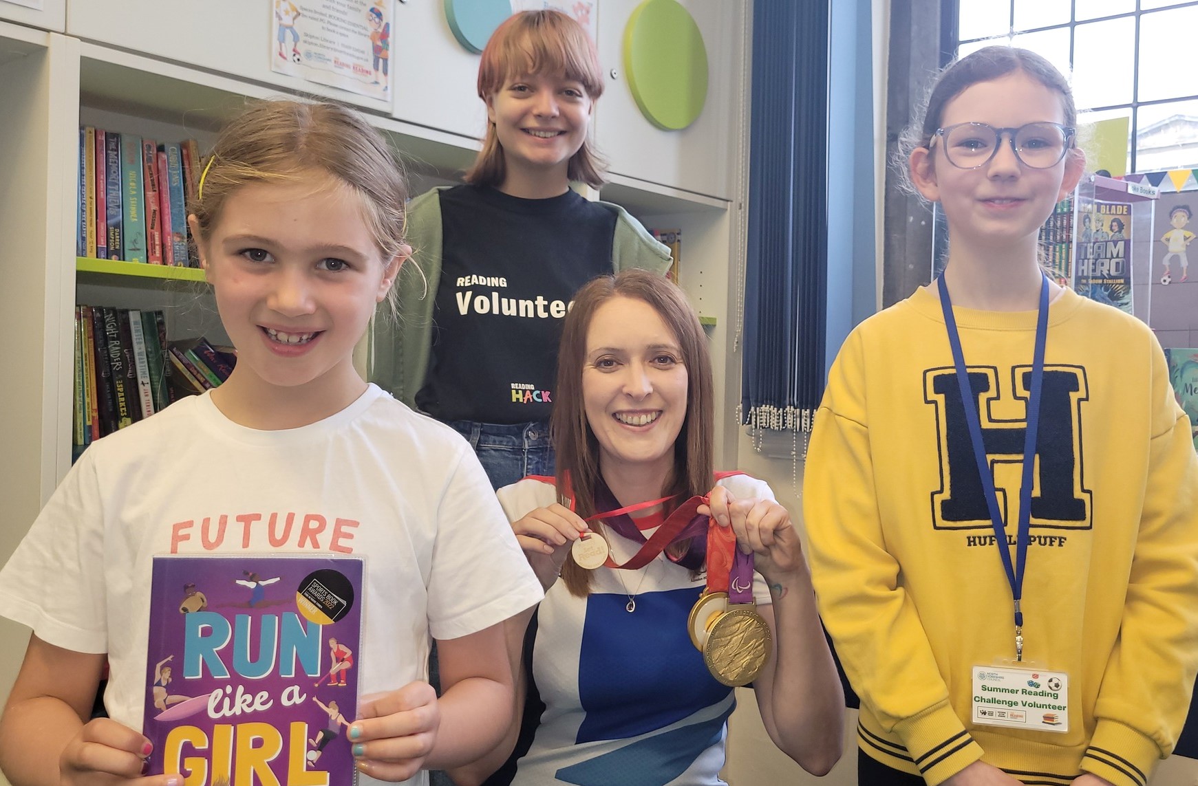 North Yorkshire-based Paralympian and author Danielle Brown wearing her gold medals and an honorary Ready, Set, Read medal, posing with two of Skipton library’s young volunteer Reading Hacks, Beth Kent, 12, and Emily Scott, 16, and Summer Reading Challenge participant Lucy Browne, seven, holding Danielle's book, Run Like a Girl.