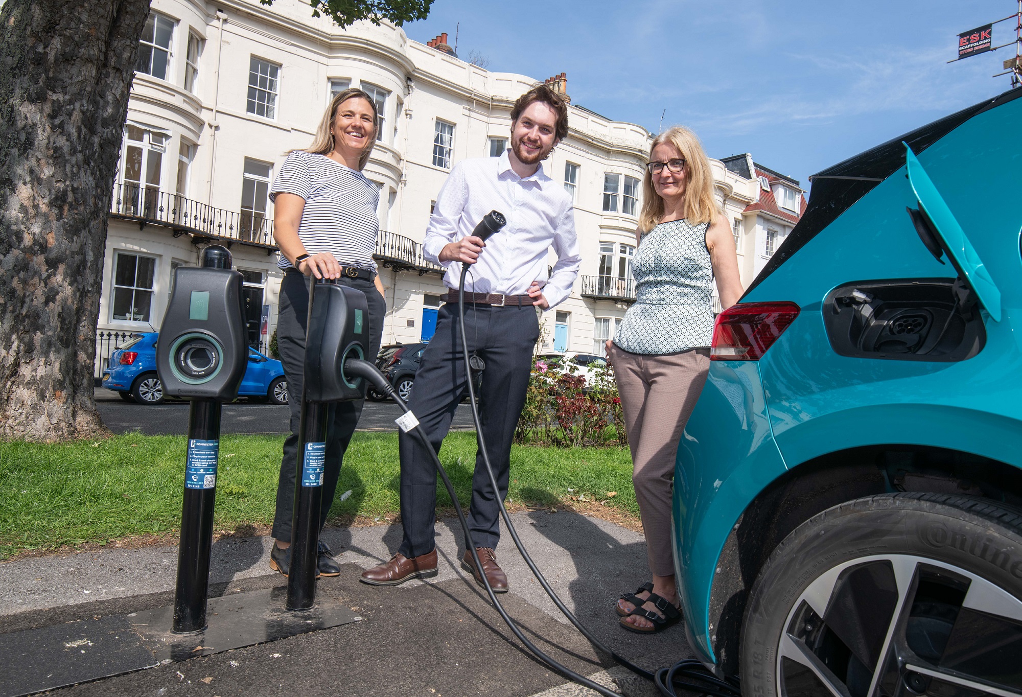 Three people with an electric vehicle at a charge point