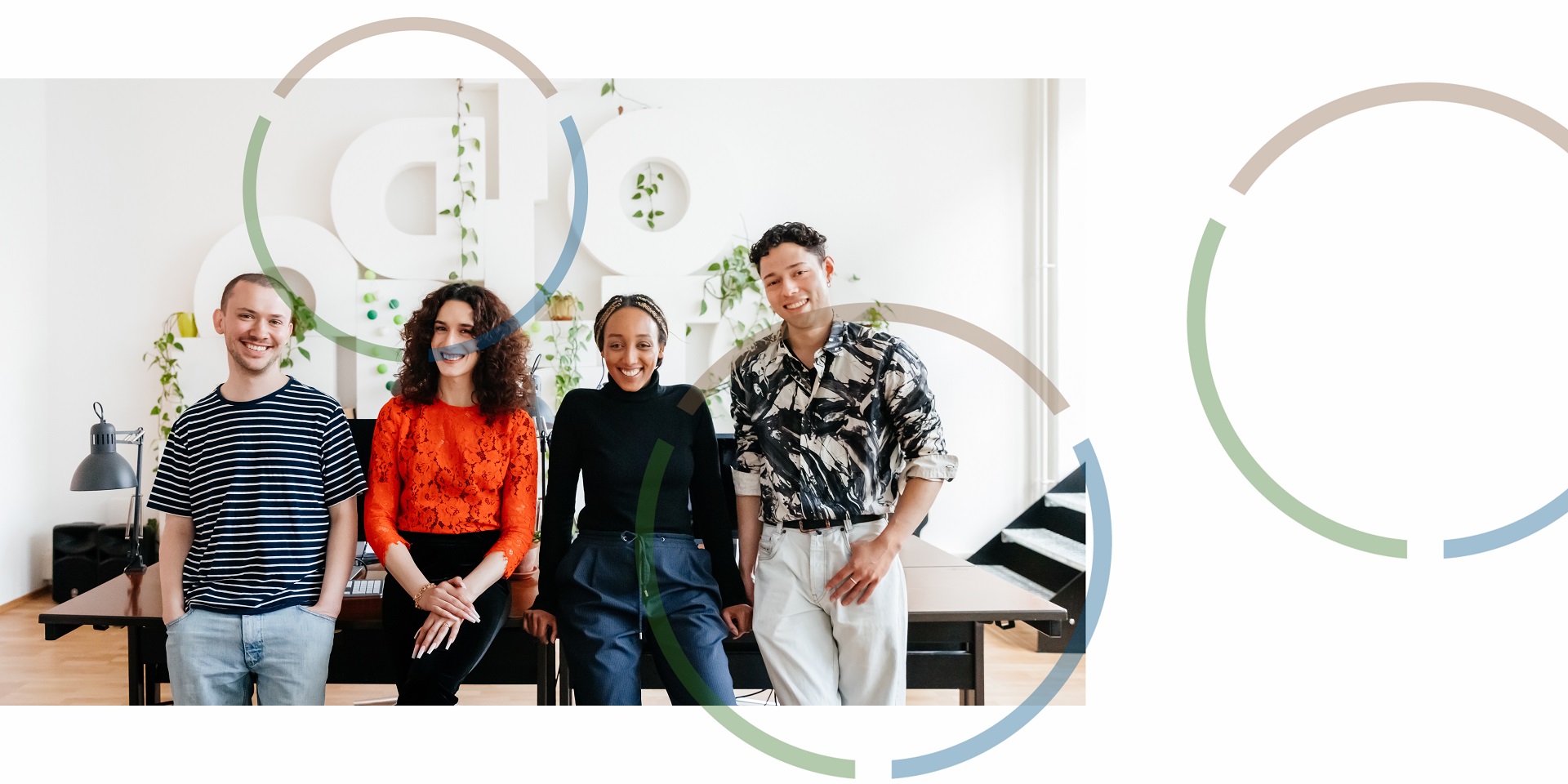 4 people smiling in a office, leaning against a desk.