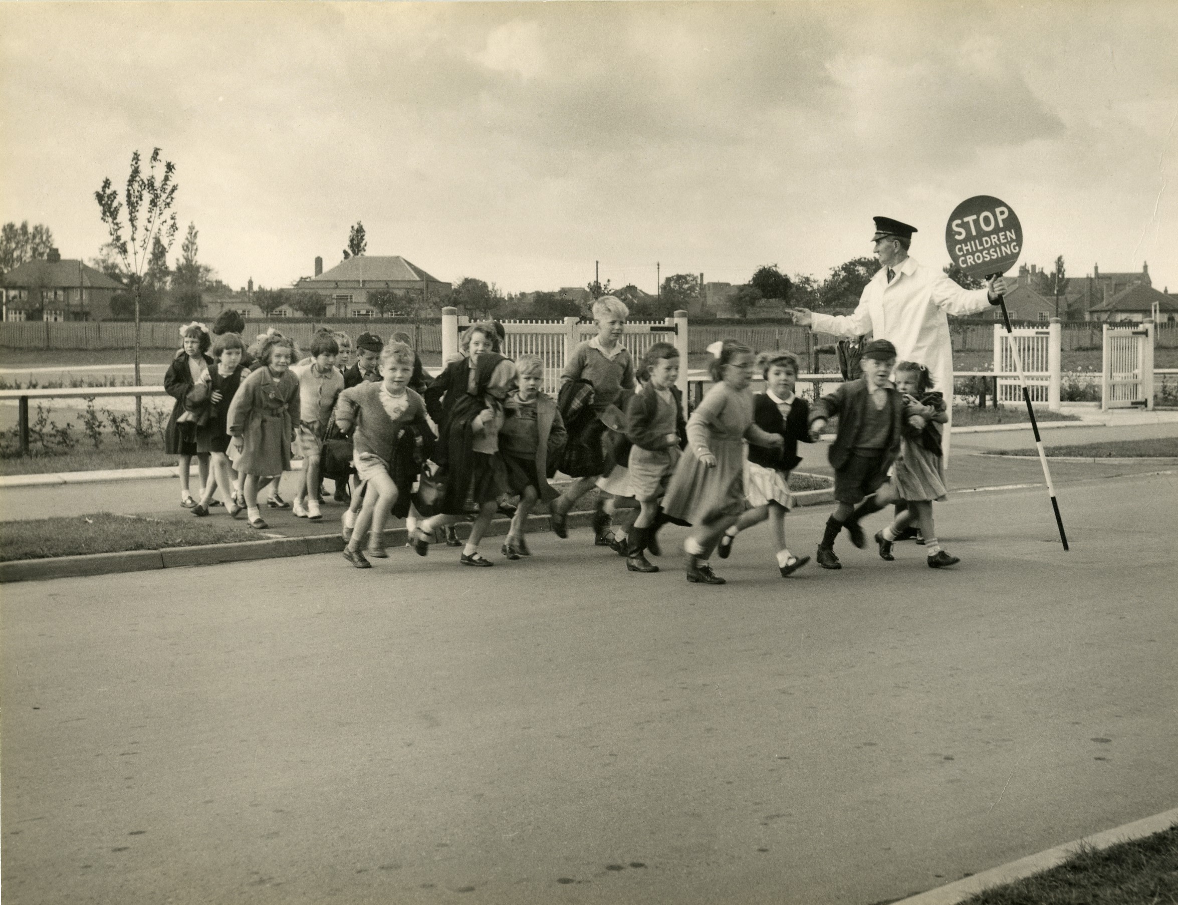 Children enthusiastically cross the road with a lollipop man at Mill Hill Junior School in 1956.