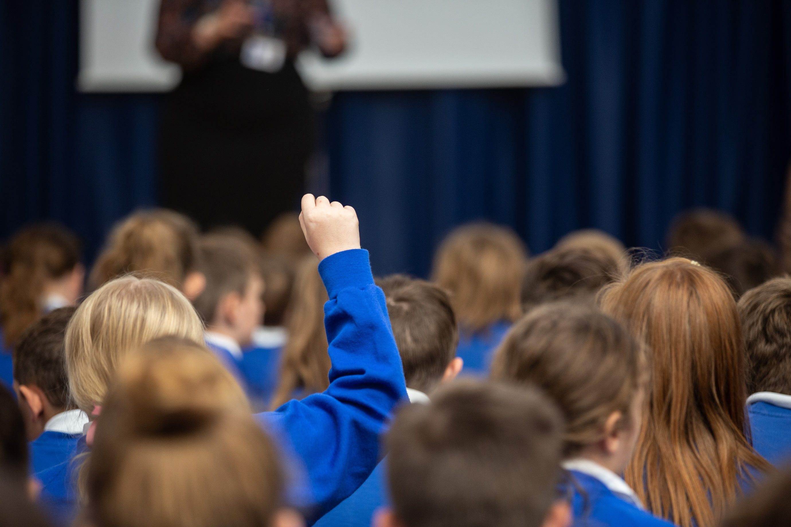 A child with their hand raised in a school assembly 