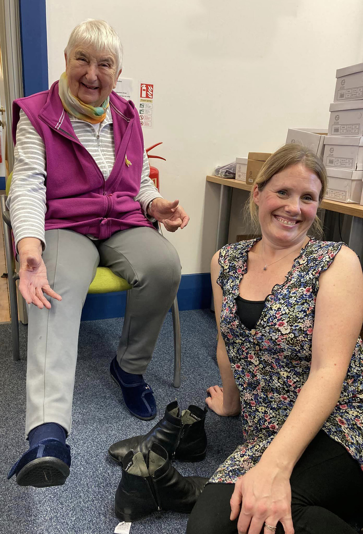 Library user Kay Piper tries on a pair of slippers with Caroline McCarthy