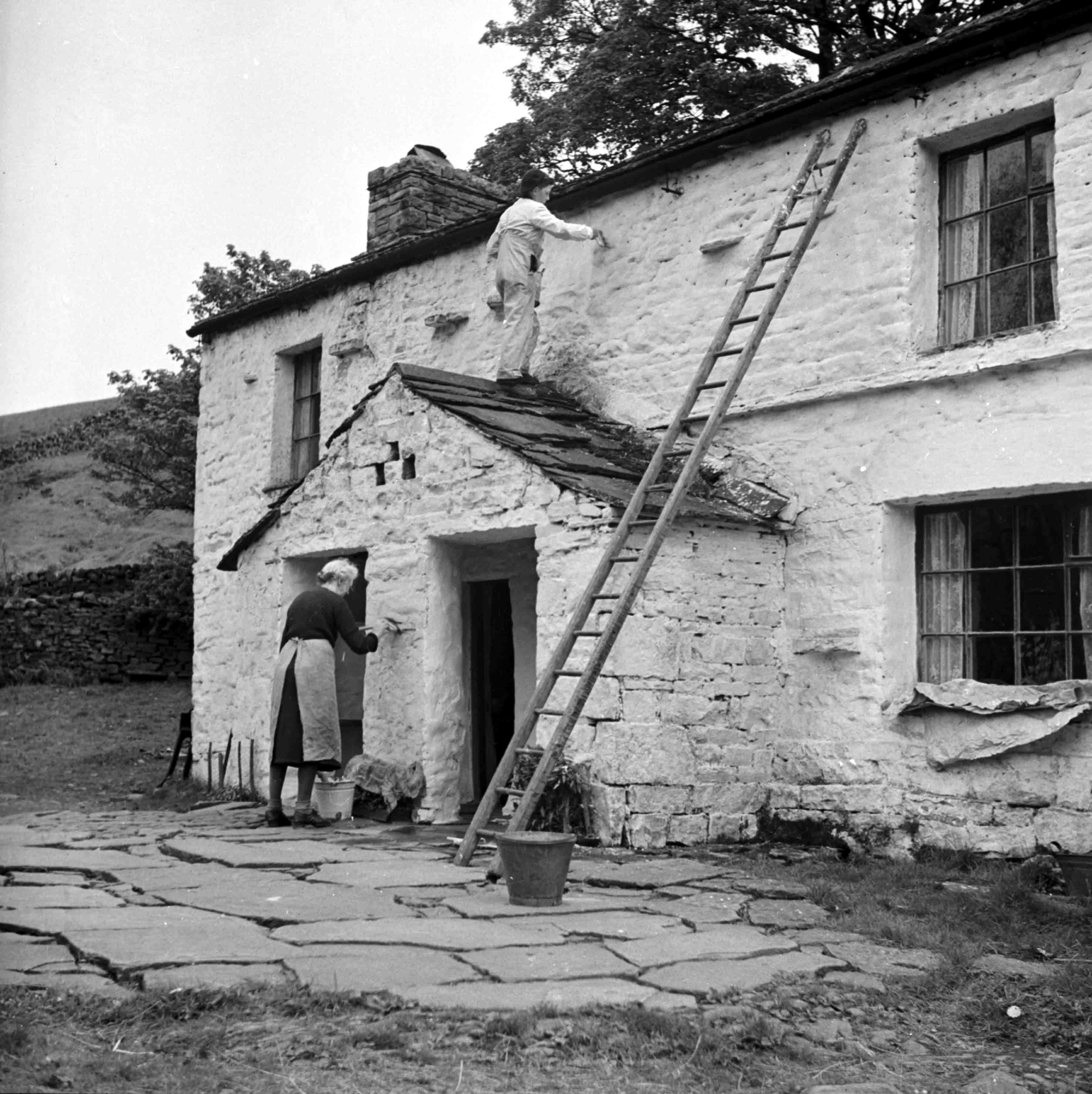 Two people hard at work in Garsdale, giving a cottage a springtime whitewash (undated). From the Bertram Unné photographic collection.
