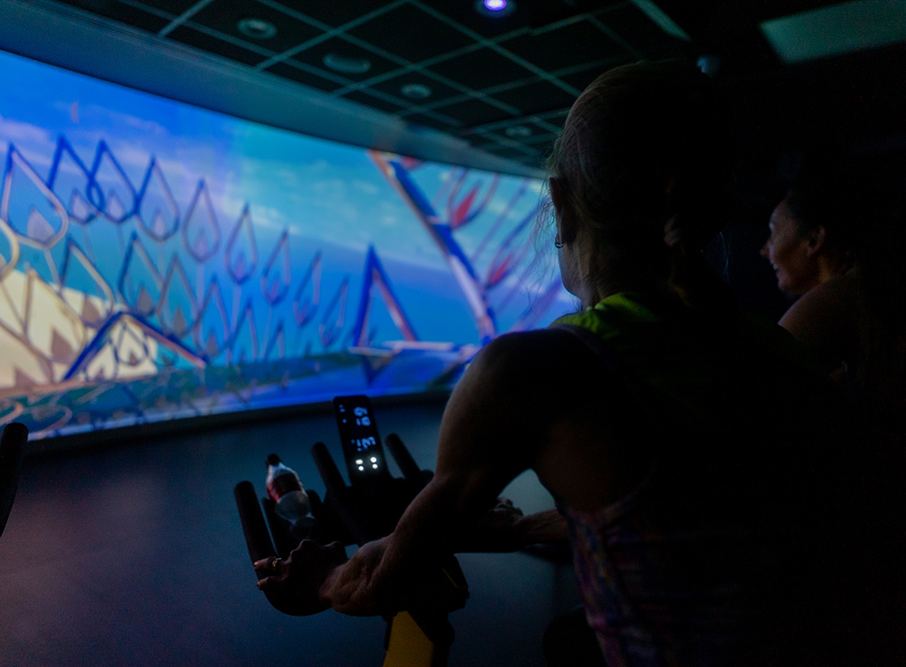 Photo of a person cycling at an exercise class in front of a large screen at Knaresborough Leisure and Wellbeing Hub
