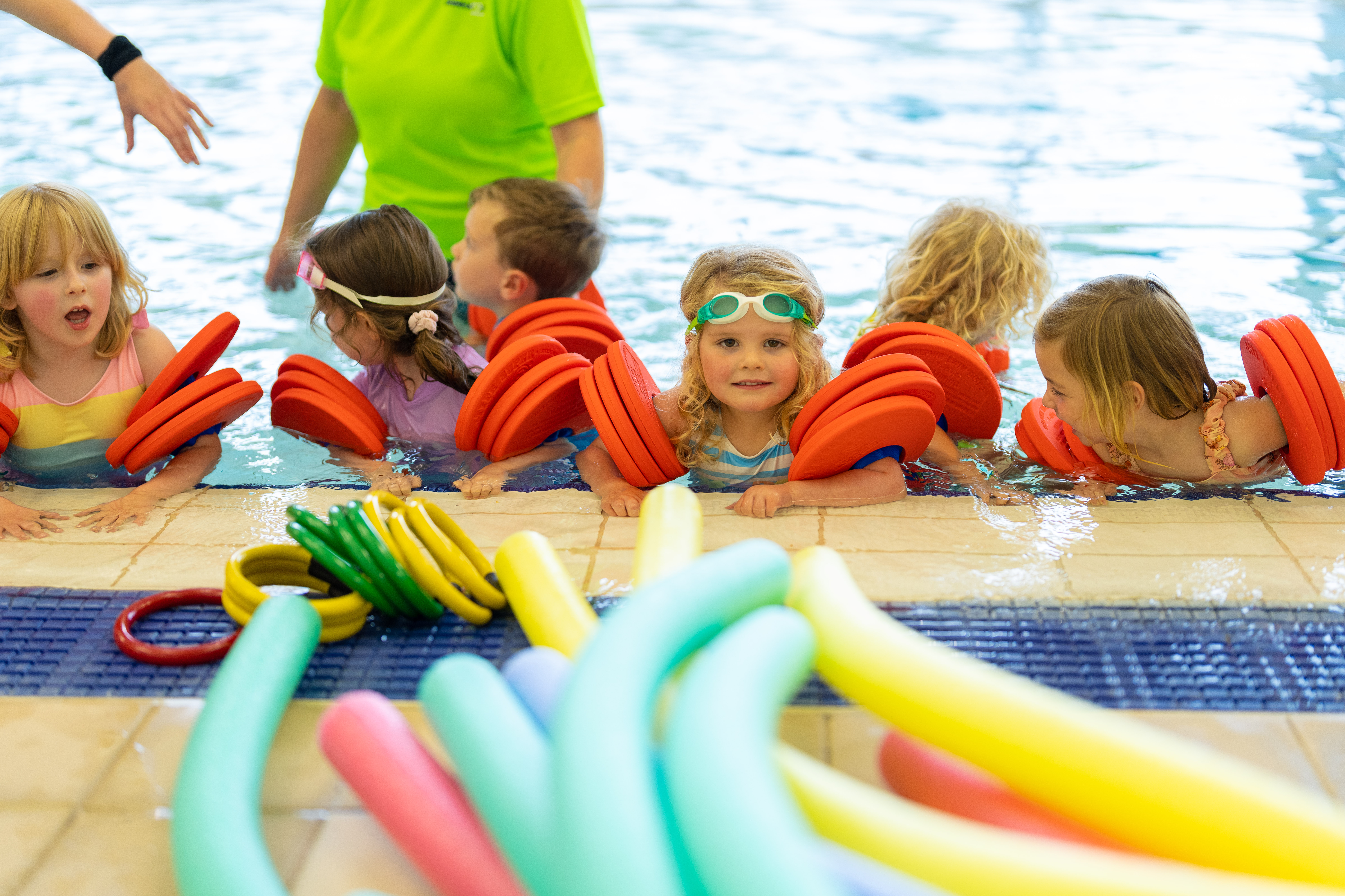 A group of children in the pool wearing arm bands beside a selection of colourful floats