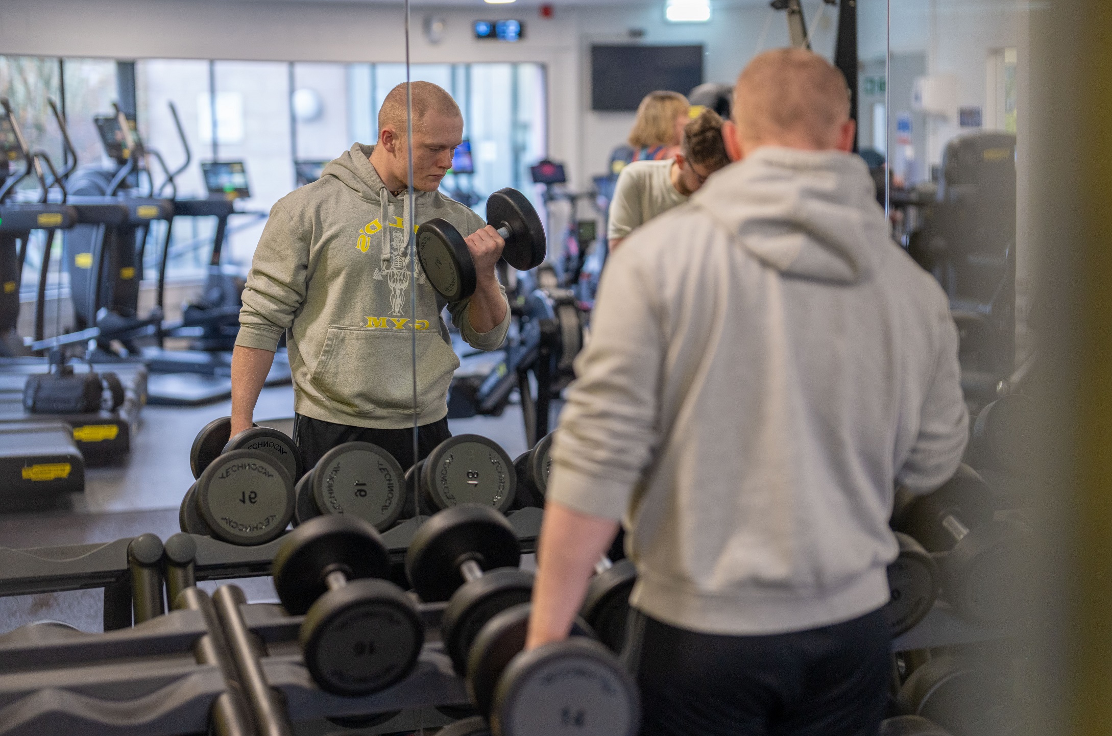 A man lifting weights in front of a mirror in the gym at Pateley Bridge Leisure and Wellbeing Hub