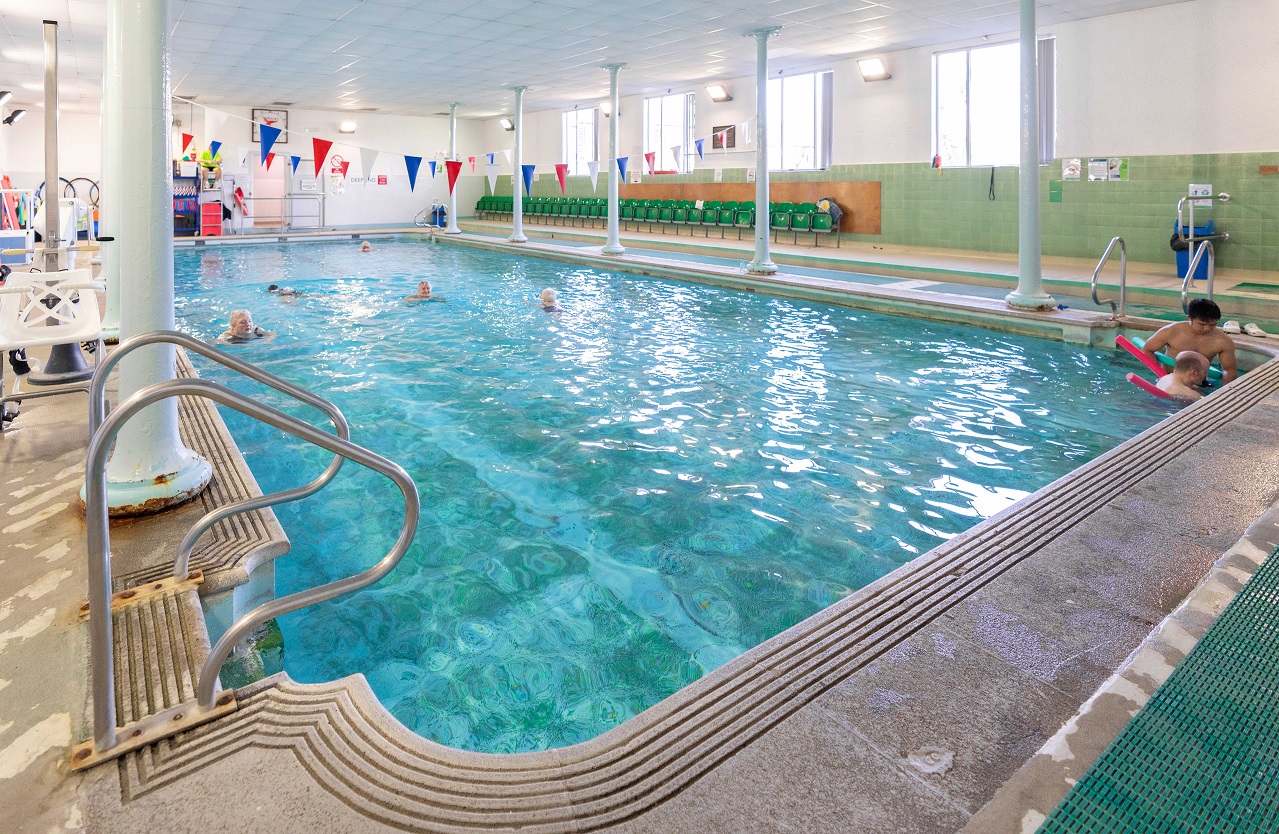 A wide view of Starbeck Swimming Pool with several people swimming and using floats