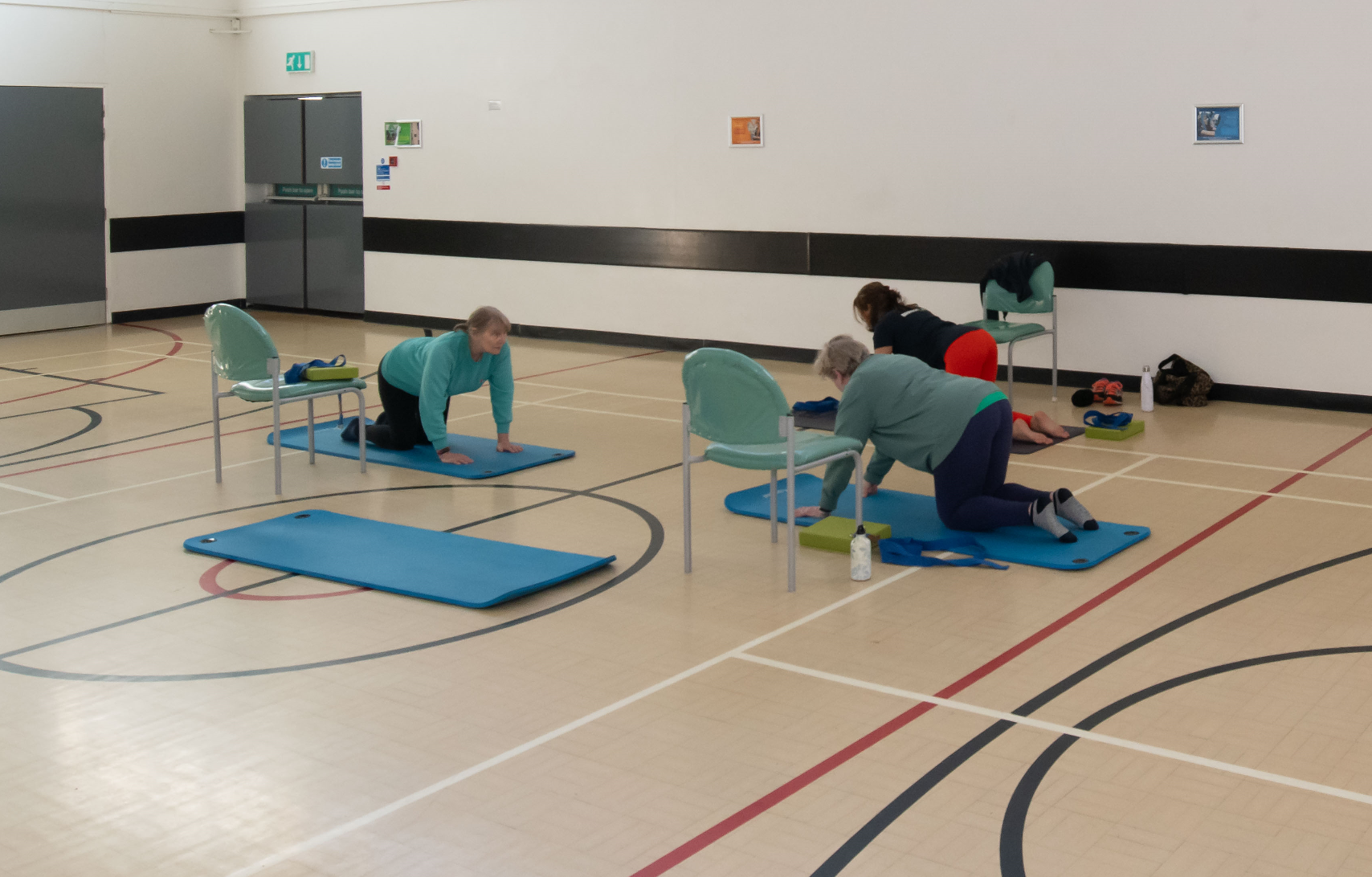 A group of women in yoga poses in the sports hall of the Stockwell Community Wellbeing Hub 