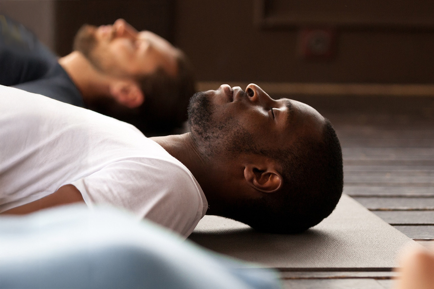 Three people laying down on a mat with their eyes closed.