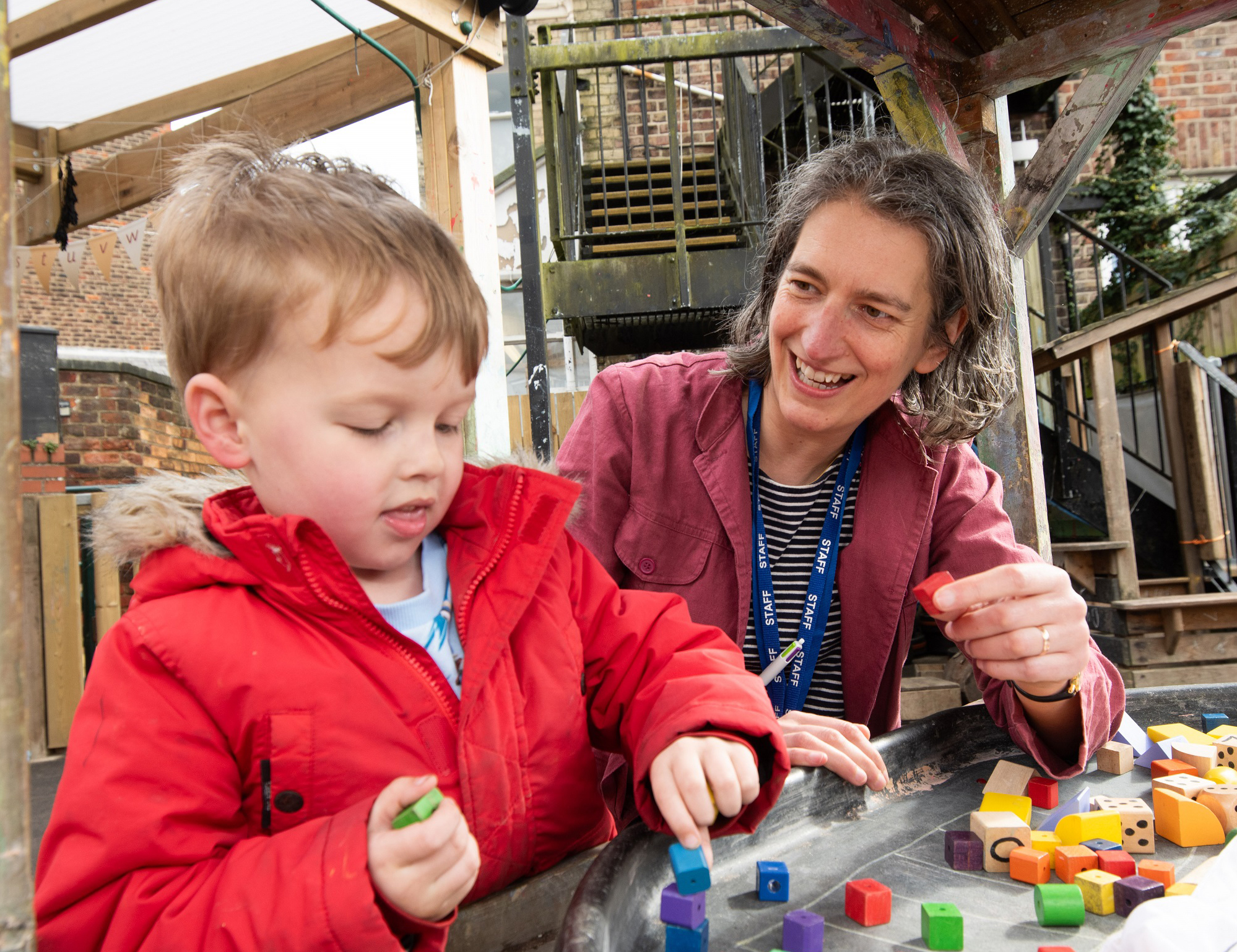 Child with teacher enjoying playing with colourful building blocks outside.