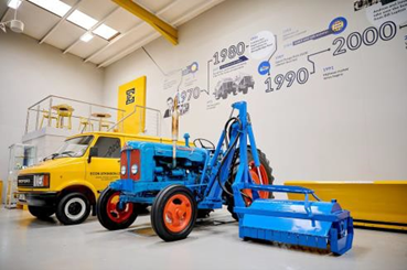 Photo of a yellow van and a blue tractor with orange wheels