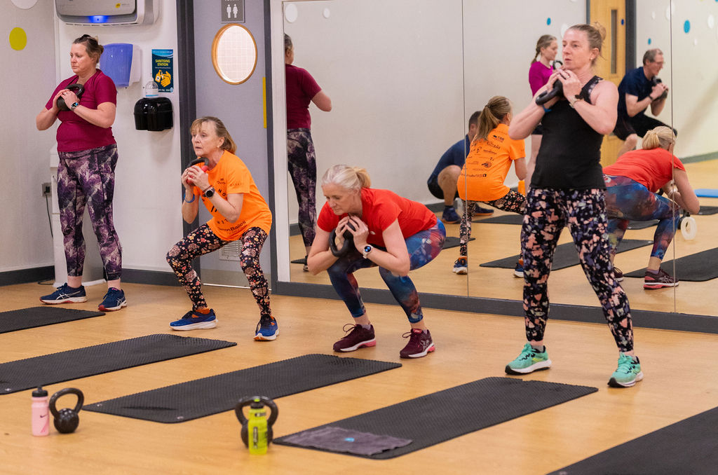 A group of women in a class performing squats while holding kettlebells