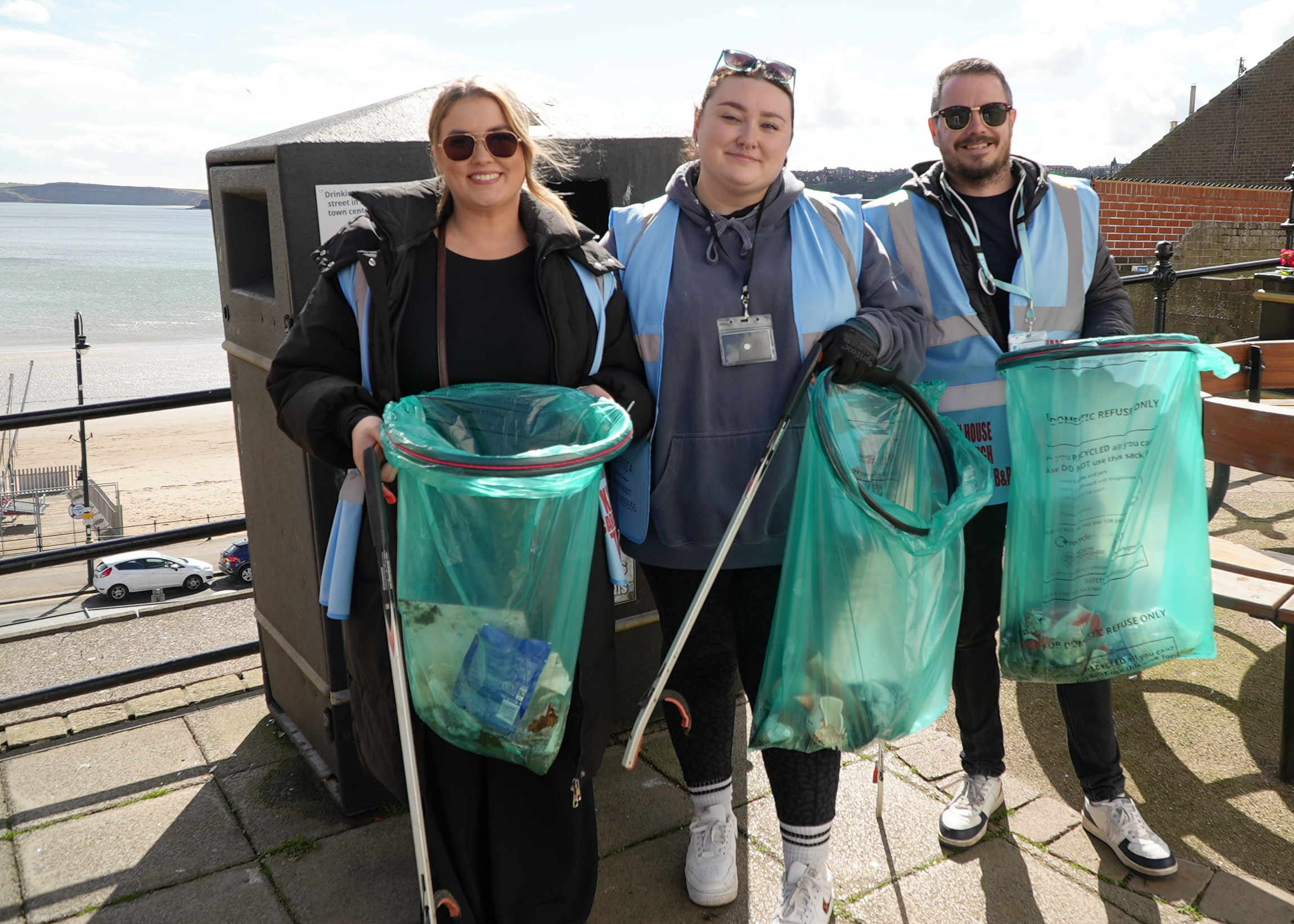 Group of people holding clear bags filled with litter with Scarborough seafront in the background