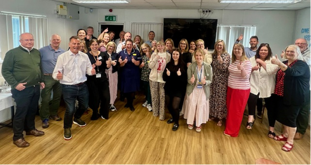 Photo of a group of people standing together with some giving a thumbs up