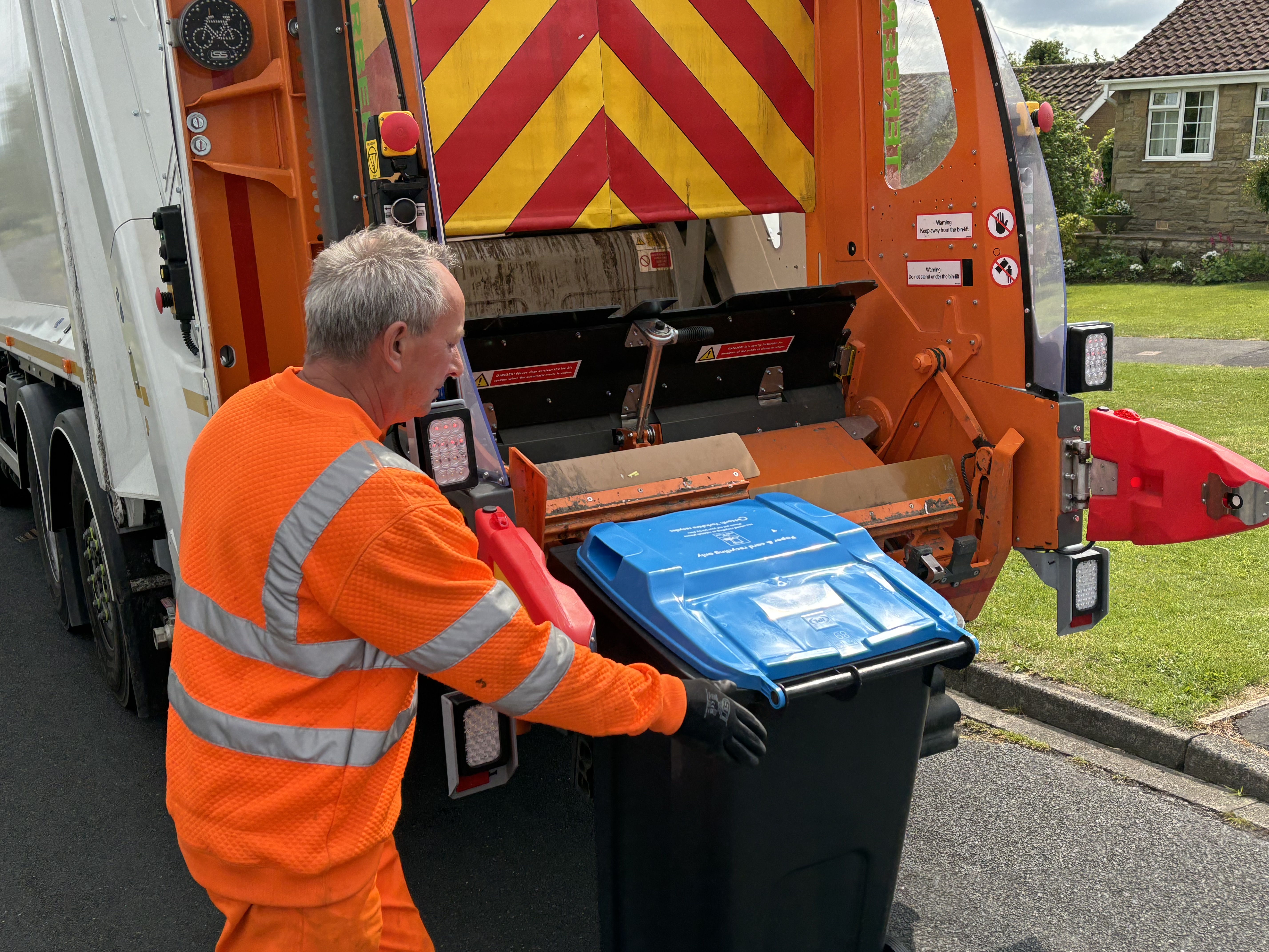 A bin man loading a bin onto a bin lorry