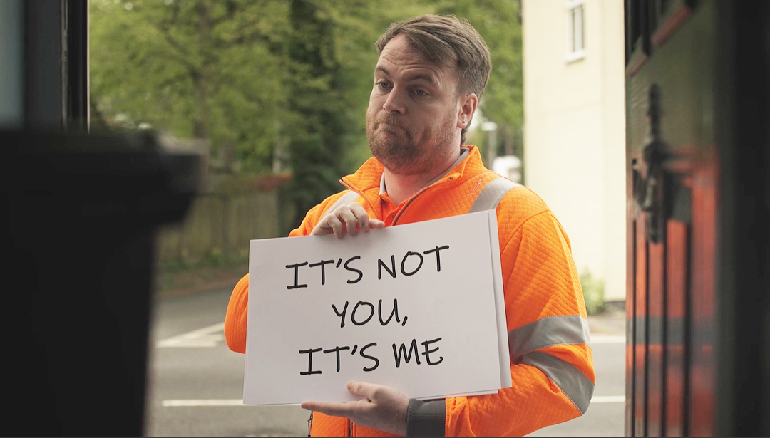Adult in an orange hi-viz jacket holding a sign saying It's not you, it's me
