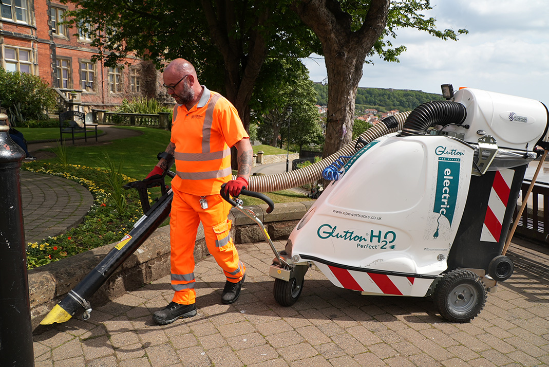 Person wearing orange hi-viz using a cleaning machine on block paving