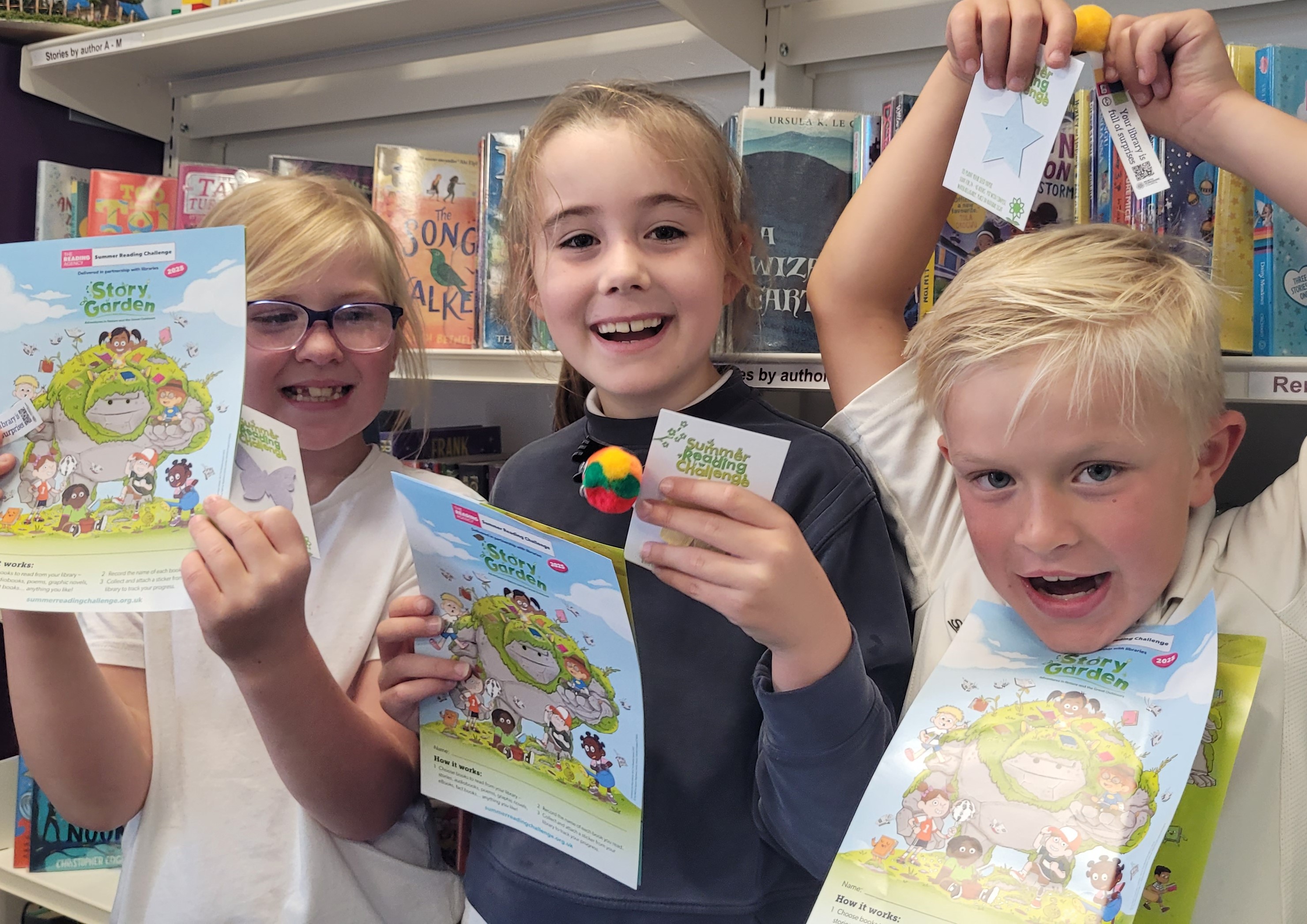 Three children smiling holding a Story Garden booklets