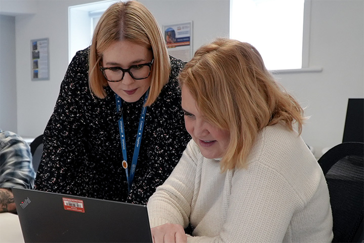Adult learner on laptop next to a teacher