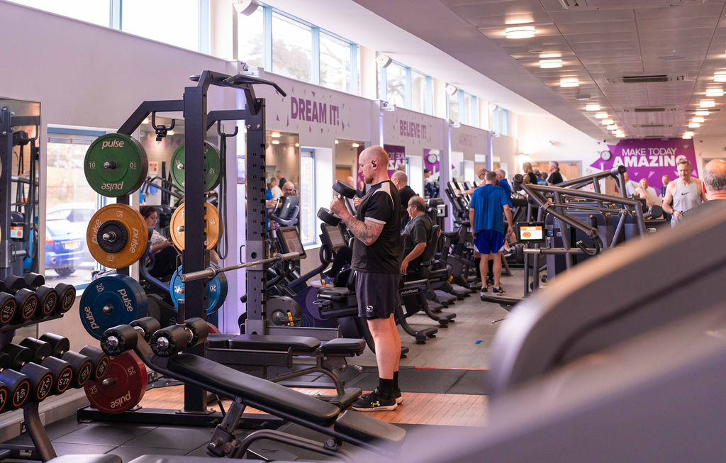 A man lifts weights in the centre of Skipton Leisure and Wellbeing Hub's gym, he is surrounded by gym equipment which others are using in the background.
