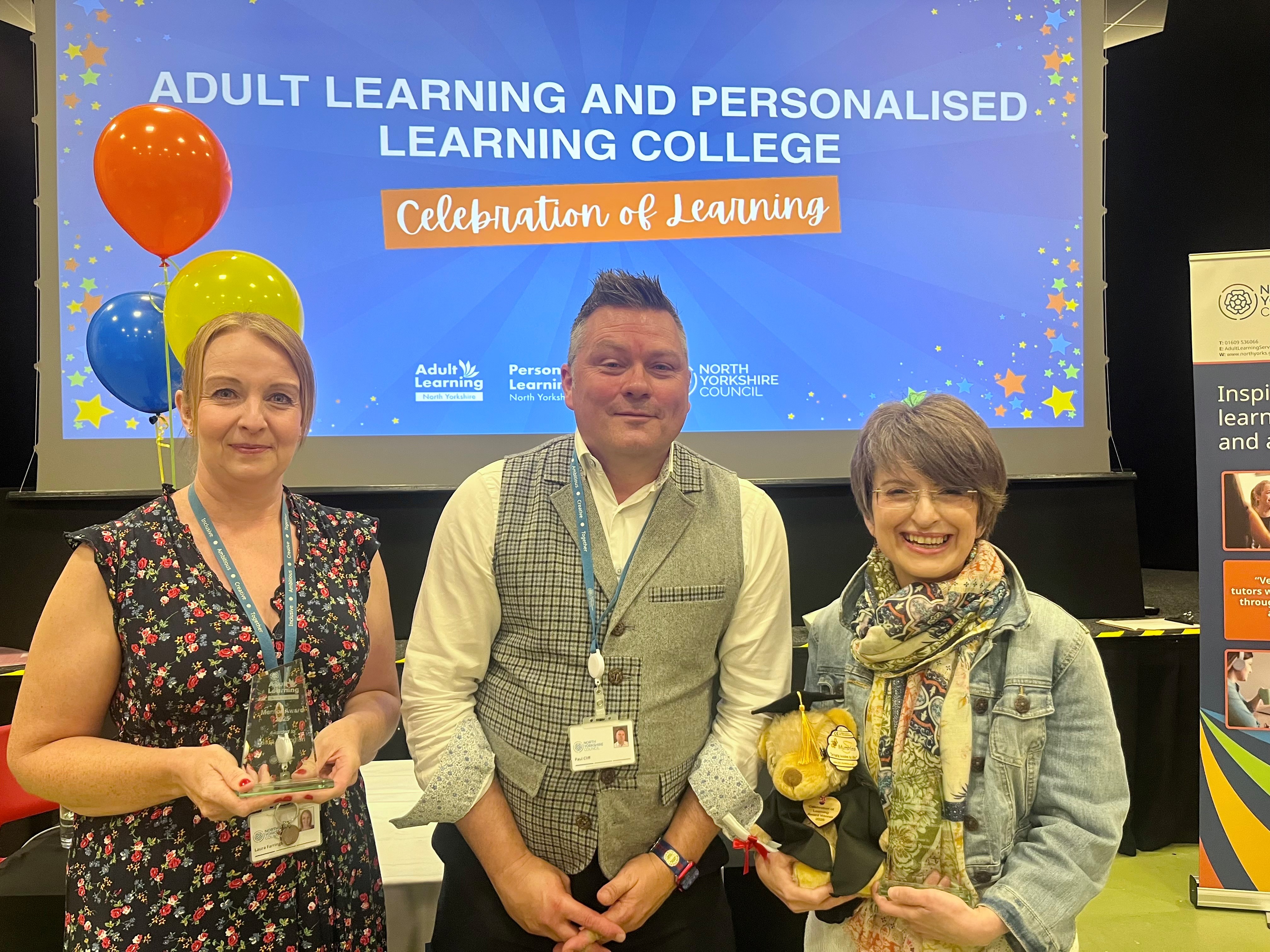 Three adults smiling in front of a celebration of learning screen behind them