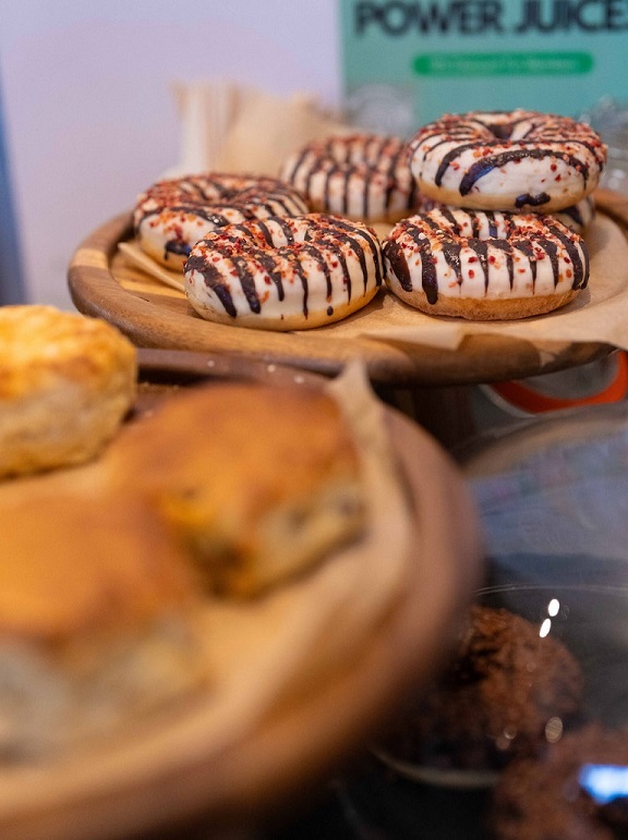 A pile of doughnuts with brown and cream striped icing. In the foreground, scones are visible.