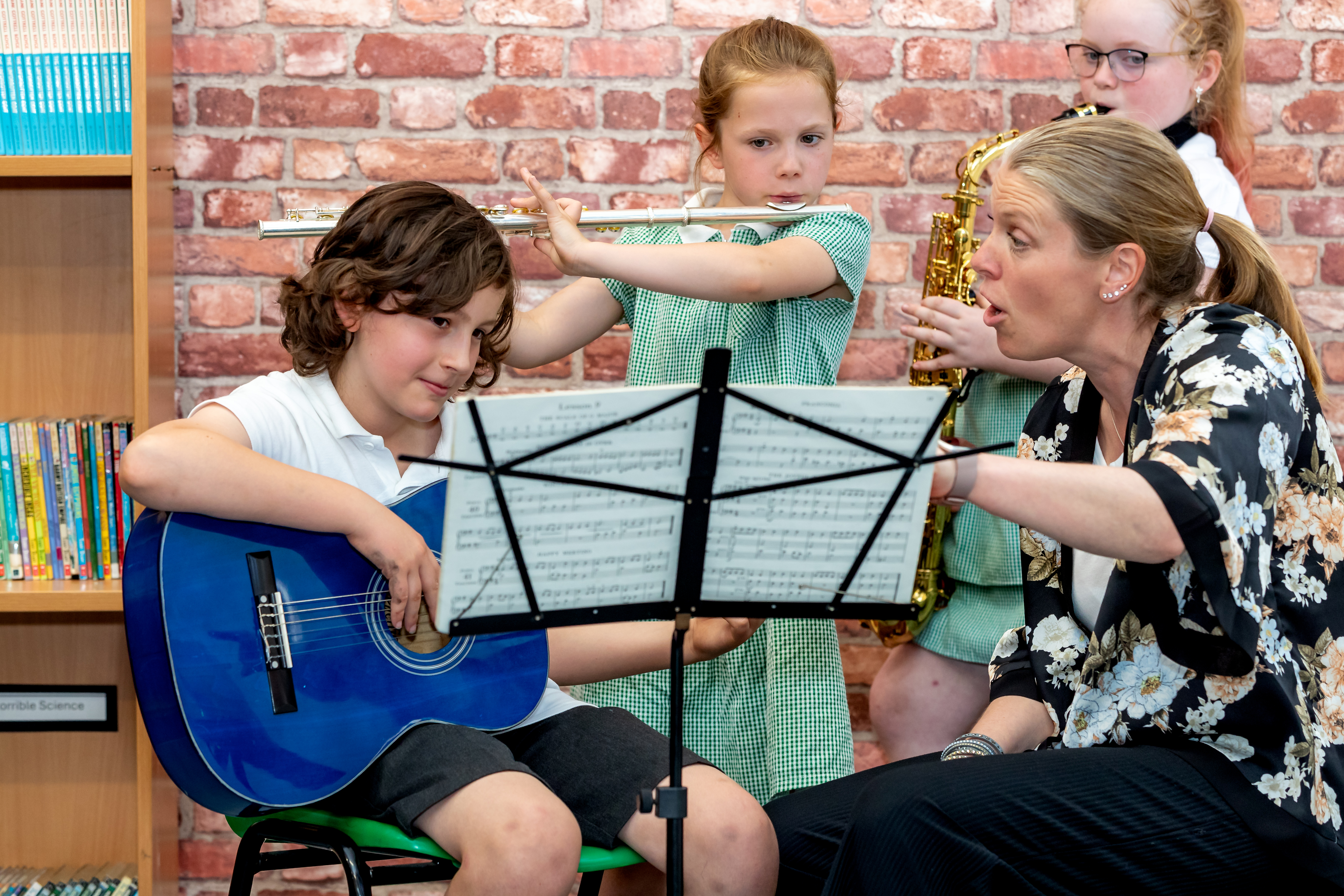 Children playing guitar, flute and saxophone during a music lesson with their teacher.
