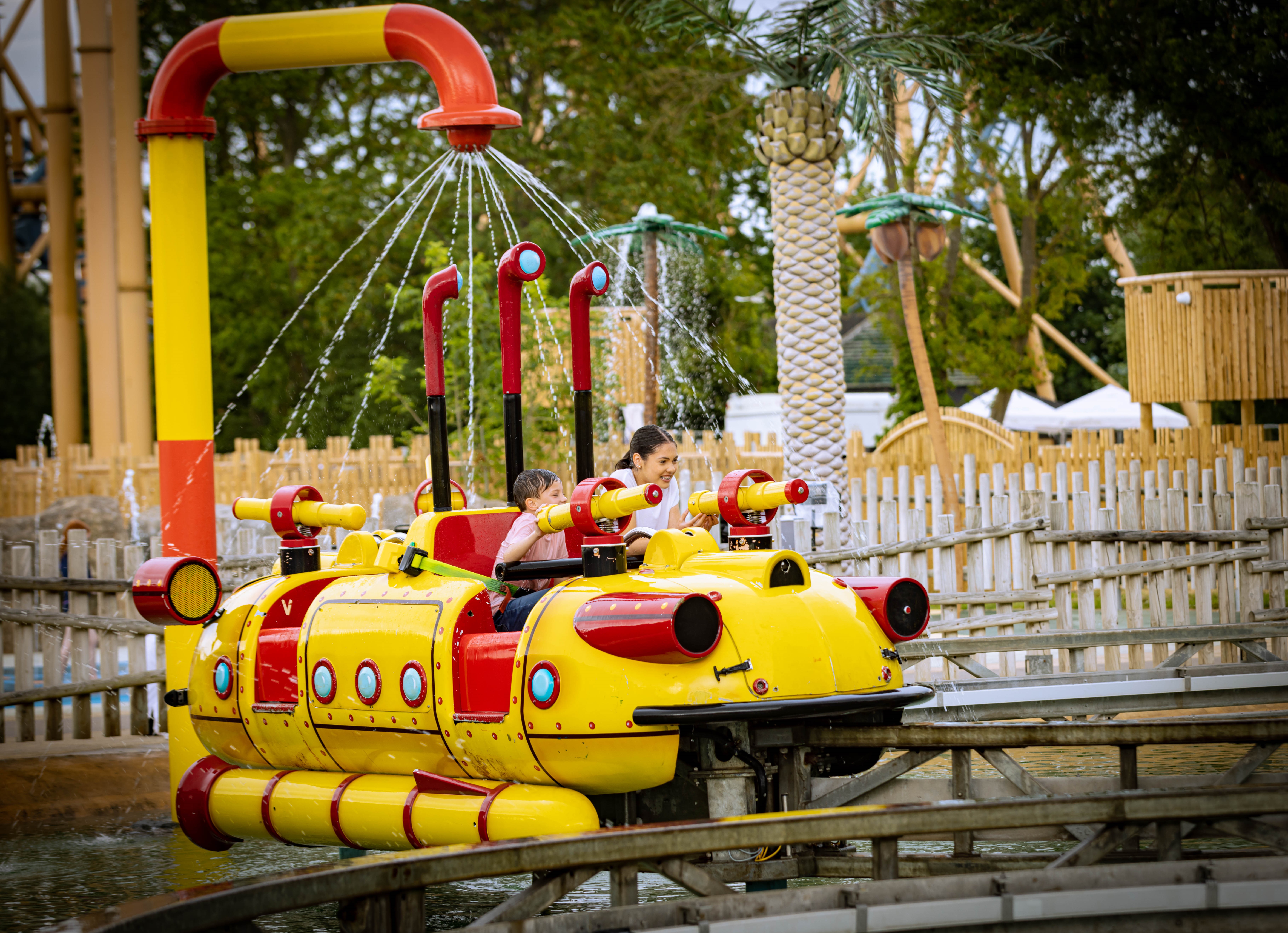 Two children sitting in a yellow and red submarine getting wet on a ride at Flamingo Land