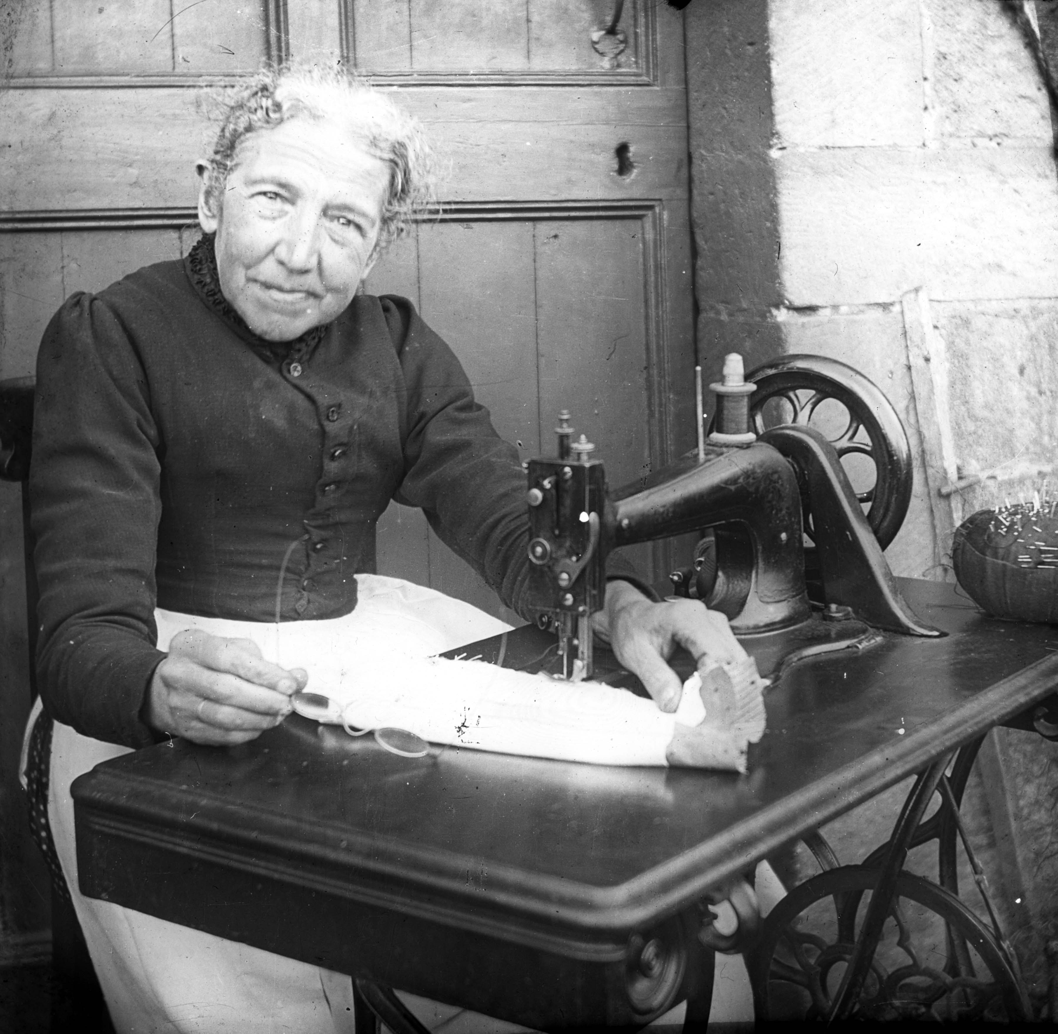 A woman busy at her treadle sewing machine.