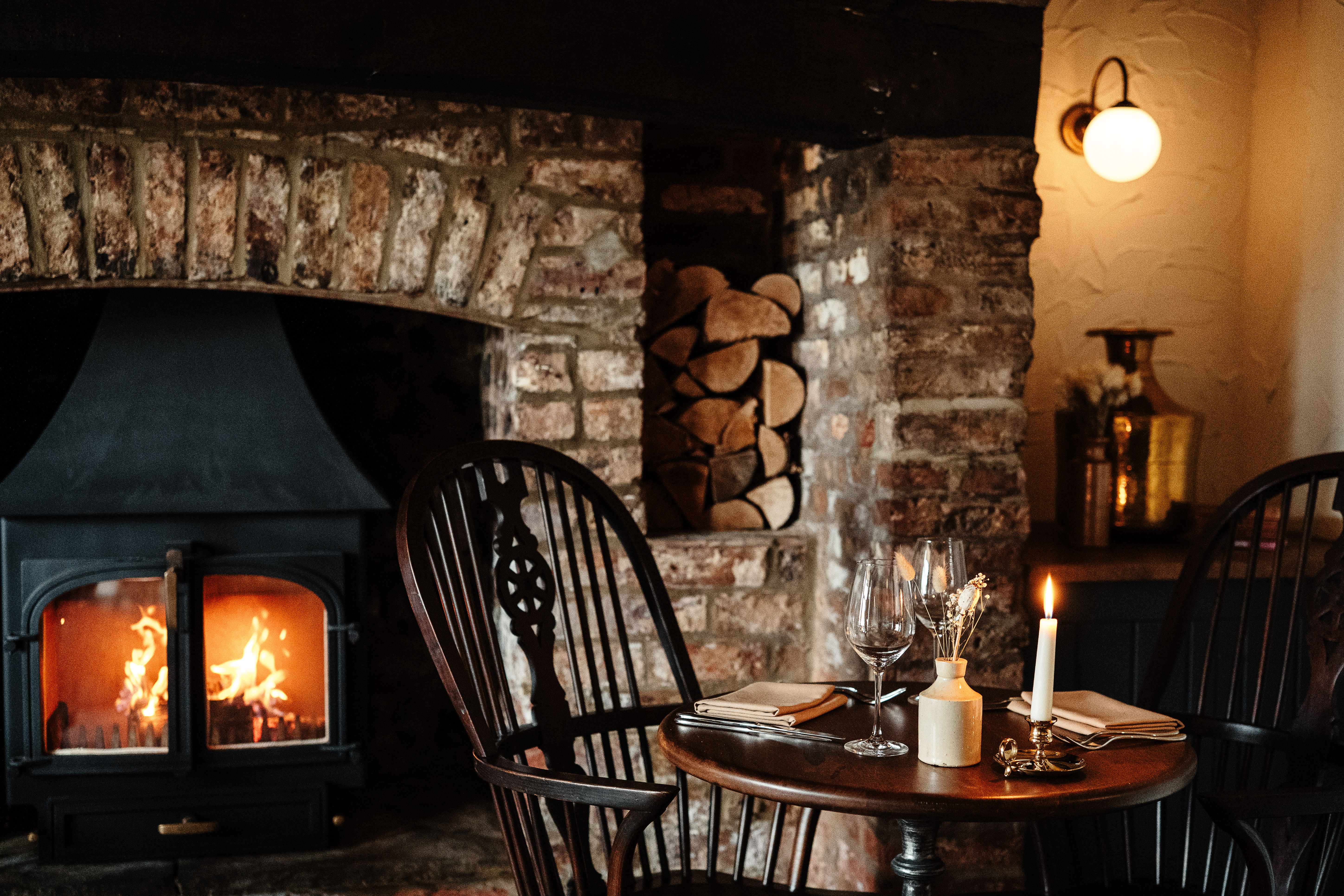 Lit log burner inside Tarleton Inn with set table with glasses and lit candle