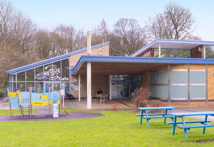 The outside of Skipton Leisure and Wellbeing Hub and Revive Cafe, a play park and picnic tables are visible in the foreground.