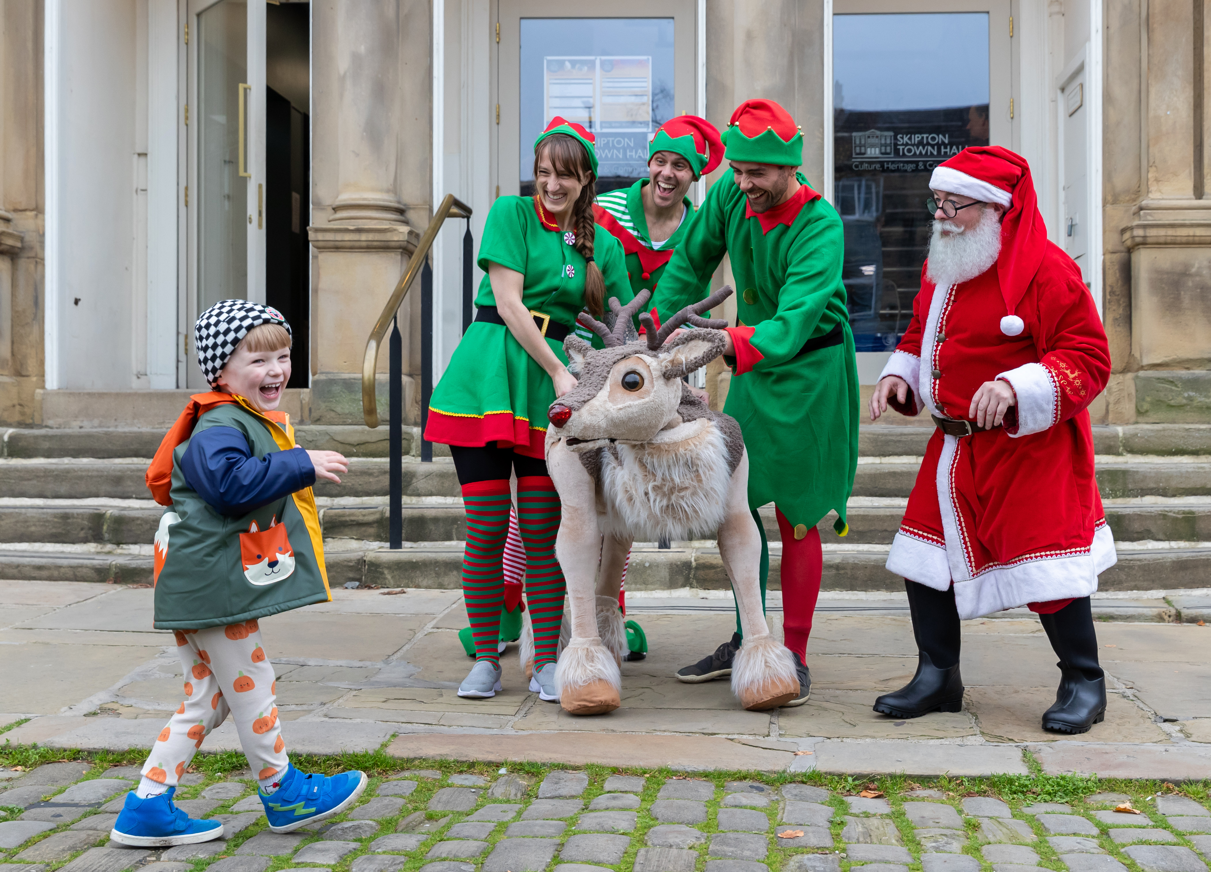 Santa and his elves and reindeer standing outside Skipton Town Hall with a child smiling with them