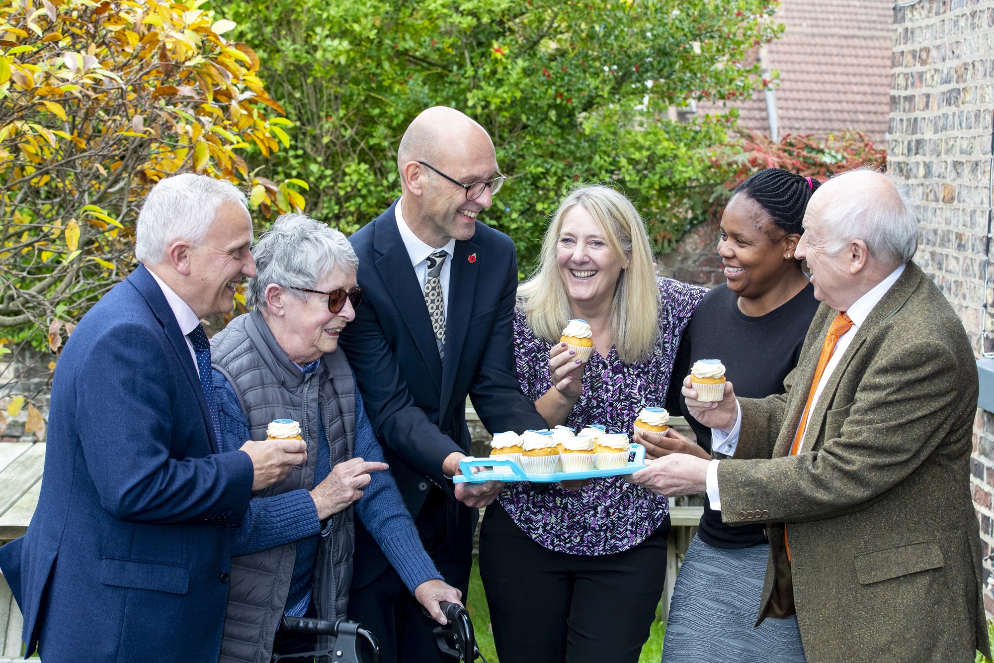 Group of adults standing outside with a tray of fairy cakes
